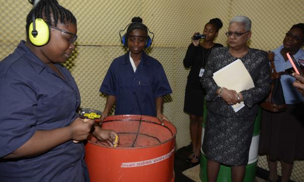 Permanent Secretary, Ministry of Education Angela Sinaswee-Gervais (right) observes a demonstration by a student of Mucurapo West Secondary School of how a steelpan is designed during a tour of the in- house pan lab.